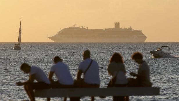A cruise ship is seen on the horizon as people tak