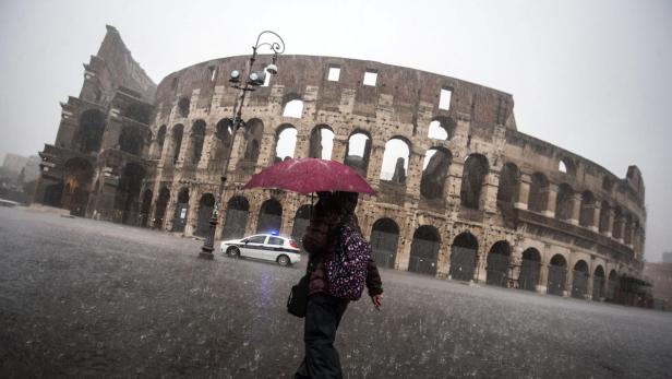 Eine Person mit Regenschirm geht im Regen am Kolosseum in Rom vorbei.