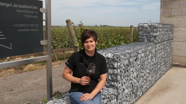 Eine Frau sitzt vor einem Weinberg und hält ein Glas Rotwein in der Hand.