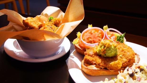 Ein offener Burger mit Guacamole und ein Schälchen mit frittierten Bällchen stehen auf einem Tisch.