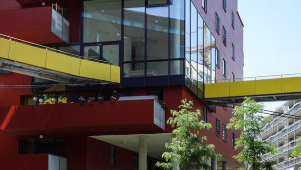 Ein rotes Gebäude mit gelben Übergängen zu einem weiteren Gebäude unter blauem Himmel.