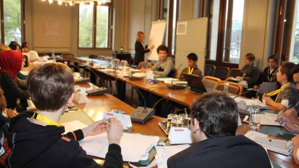 Teilnehmer sitzen an einem langen Tisch während einer Präsentation.