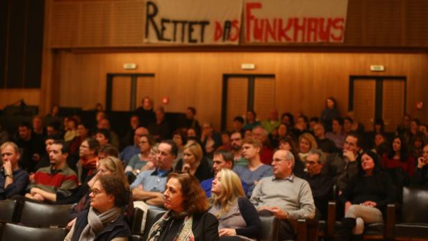 Publikum sitzt in einem Saal unter einem Banner mit der Aufschrift „Rettet das Funkhaus“.