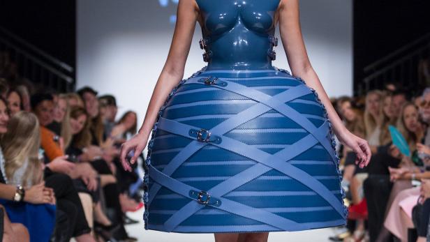 Eine Frau präsentiert ein blaues Kleid mit ungewöhnlichem Design auf einem Laufsteg.