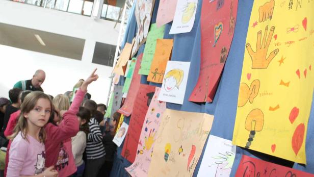 Eine Gruppe von Kindern betrachtet eine Wand mit bunten, selbstgemalten Bildern.