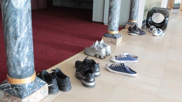 Verschiedene Schuhe stehen vor Säulen auf einem gefliesten Boden.
