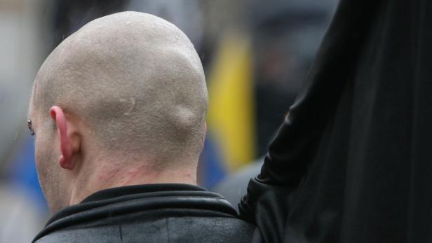 Ein Mann mit rasiertem Kopf und Ohrring, von hinten gesehen.