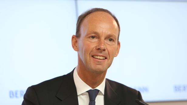 Ein lächelnder Mann im Anzug steht vor einem Mikrofon.