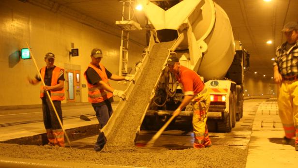Bauarbeiter verteilen Beton aus einem Betonmischer in einem Tunnel.