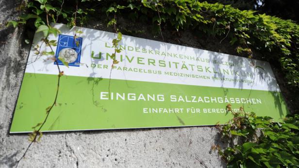 Ein Schild des Landeskrankenhauses Salzburg, teilweise von Efeu bedeckt.