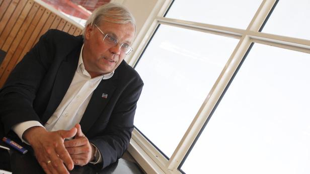 Ein Mann mit Brille und Anzug sitzt an einem Fenster.