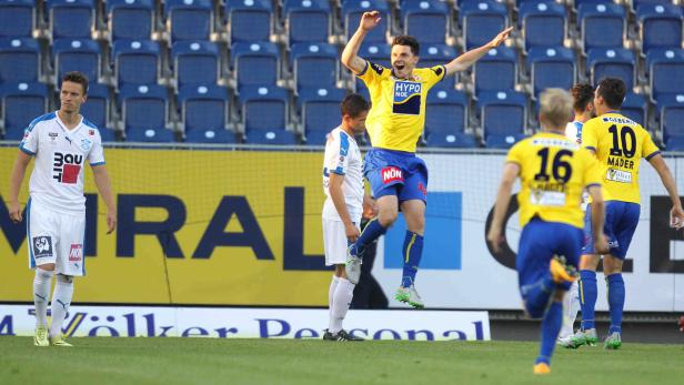 Ein Fußballspieler in gelbem Trikot jubelt mit erhobenen Armen auf dem Spielfeld.