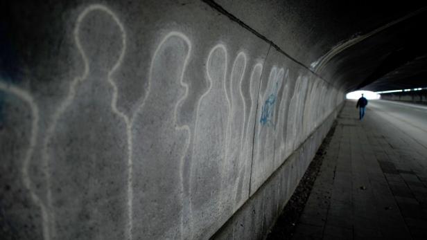 Ein Mann geht in einem Tunnel entlang einer Wand mit Graffiti-Umrissen von Menschen.