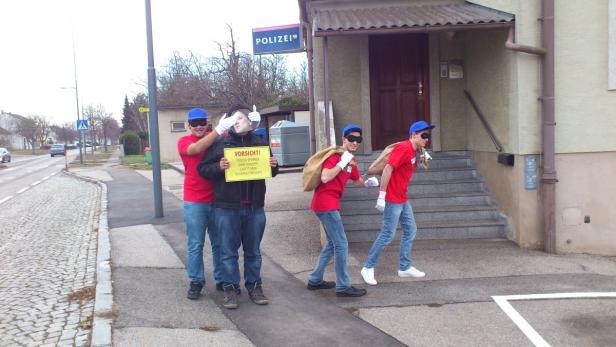 Eine Gruppe von Personen verkleidet als Diebe vor einer Polizeistation mit einem Schild, das vor Sicherheitsrezepten warnt.