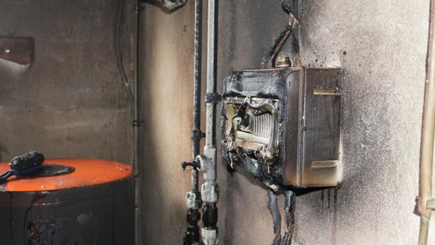 Ein durch einen Brand beschädigter Sicherungskasten und ein Boiler in einem Raum.