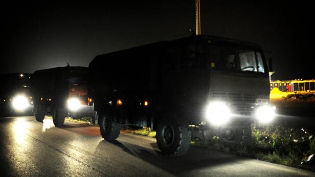 Mehrere Militärlastwagen fahren nachts auf einer Straße.