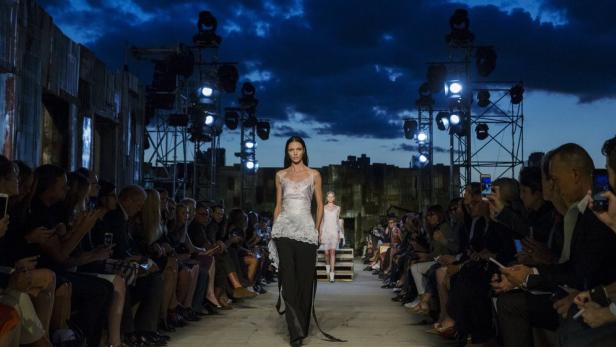 Eine Modenschau mit Models, die vor Publikum über den Laufsteg gehen.