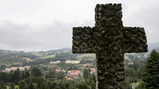 Ein Steinkreuz überblickt eine grüne Landschaft mit einer kleinen Stadt.