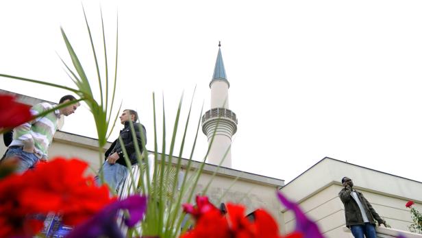 Drei Männer stehen vor einer Moschee, rote Blumen im Vordergrund.
