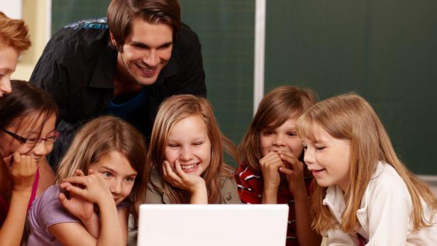 Eine Gruppe von Schülern und ein Lehrer schauen gemeinsam auf einen Laptop.