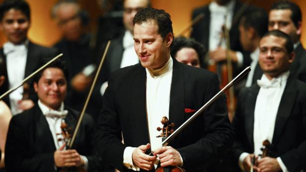 Ein Geiger lächelt inmitten eines Orchesters.