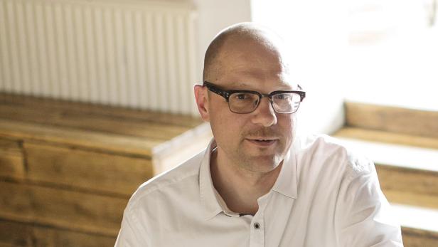 Ein Mann mit Brille und weißem Hemd sitzt auf einer Holztreppe.