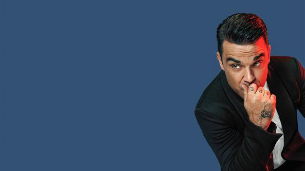 Porträt von Robbie Williams im schwarzen Anzug, der nachdenklich an seiner Hand kaut.