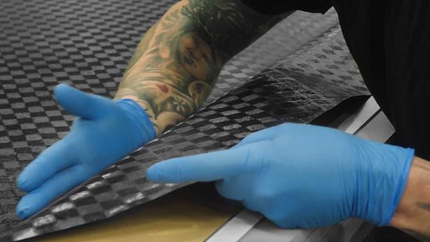 Eine Person mit blauen Handschuhen hantiert mit einem Stück Karbonfasermaterial.