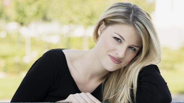 Eine lächelnde Frau mit blonden Haaren und einem Nasenpiercing blickt in die Kamera.