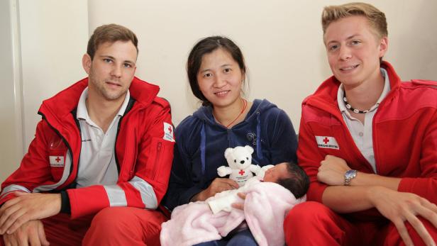 Eine Frau hält ein Neugeborenes im Arm, flankiert von zwei Mitarbeitern des Deutschen Roten Kreuzes.
