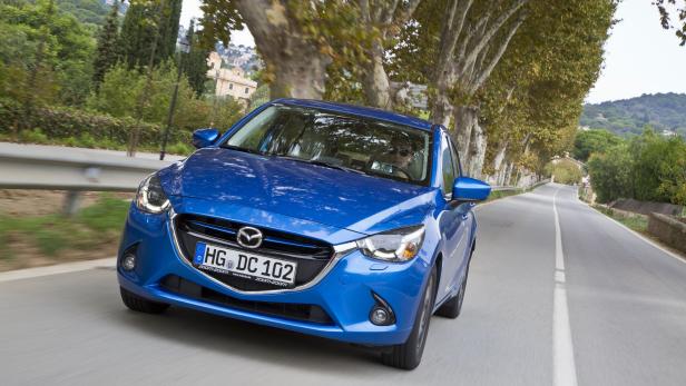 Ein blauer Mazda fährt auf einer von Bäumen gesäumten Straße.
