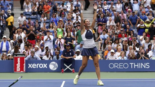 Eine Tennisspielerin jubelt mit erhobenen Armen vor einer Zuschauermenge.