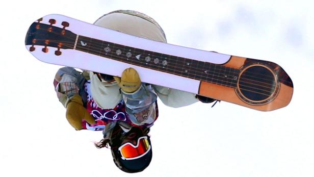 Ein Snowboarder mit einem Snowboard, das wie eine Gitarre aussieht, in der Luft.
