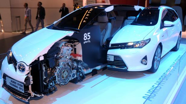 Ein weißer Toyota Auris Hybrid Touring Sports mit freigelegtem Motor auf einer Ausstellung.
