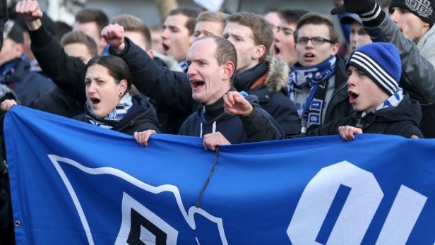 Eine Gruppe von Fußballfans hält ein blaues Banner und jubelt.