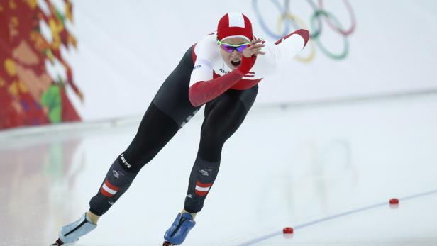 Eine Eisschnellläuferin in rot-weißer Sportkleidung auf einer Eisbahn.