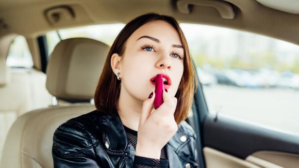 Fashion woman making up her lips with red lipstick in car