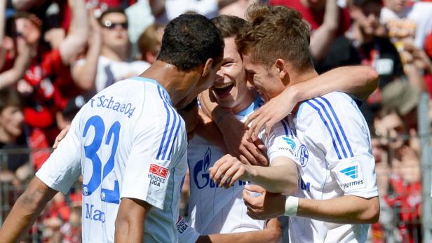 Drei Fußballspieler des FC Schalke 04 umarmen sich und jubeln.