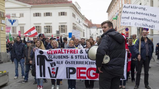 Eine Demonstration mit einer Gruppe von Menschen, die ein Banner mit der Aufschrift „Gewaltfrei & V Glaubens- & Stell auf Österreichisch“ tragen.