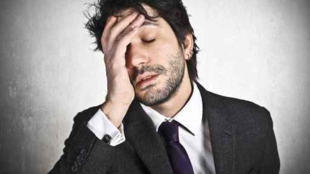 Ein Mann im Anzug hält sich mit der Hand an die Stirn.