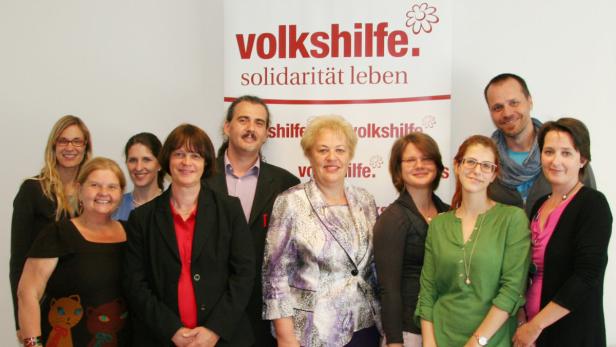Eine Gruppe von elf Personen posiert vor einem Banner der Volkshilfe.