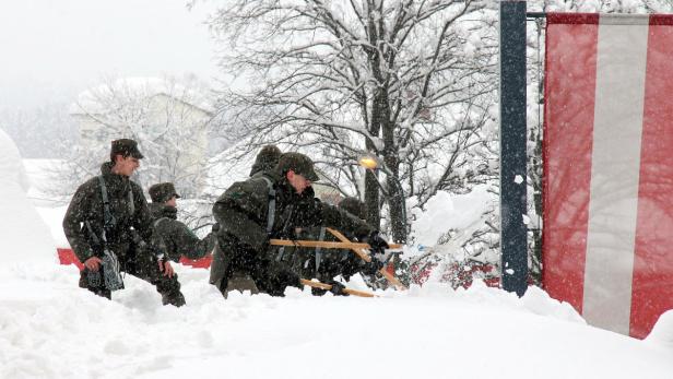 Soldaten schaufeln im Schnee vor einer rot-weiß gestreiften Flagge.