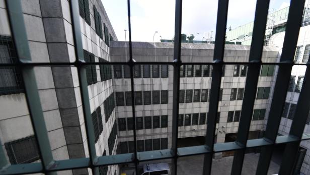 Blick durch ein Gitter auf ein mehrstöckiges Gebäude mit vergitterten Fenstern.