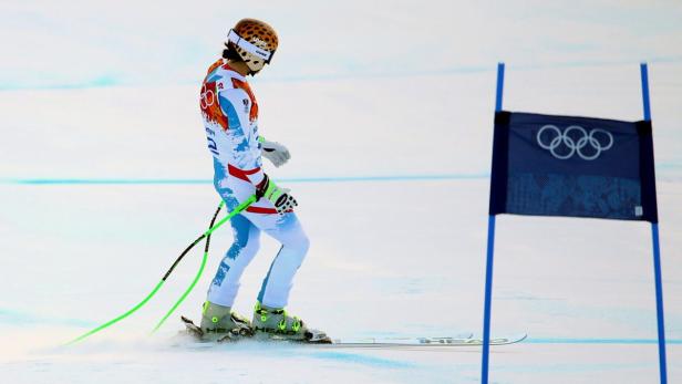 Ein Skirennläufer mit Leopardenmuster-Helm steht neben einer olympischen Fahne.