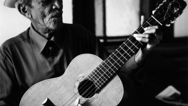 Ein älterer Mann mit Hut spielt Gitarre.