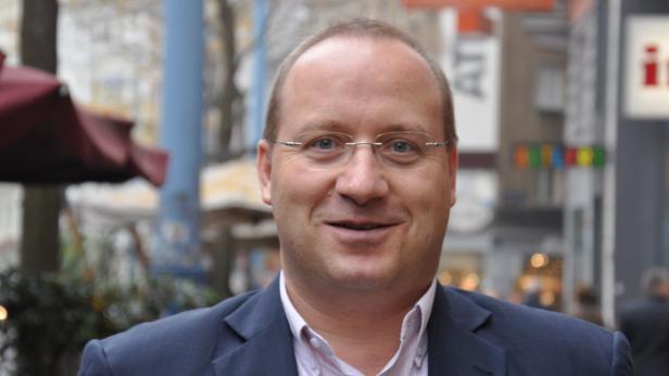 Ein Mann mit Brille und Anzug lächelt in die Kamera.