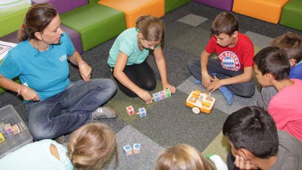 Eine Frau sitzt mit einer Gruppe von Kindern auf dem Boden und spielt mit Bauklötzen.