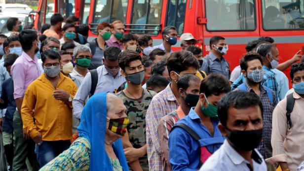 People wait to board passenger buses during rush hour at a bus terminal, in Mumbai
