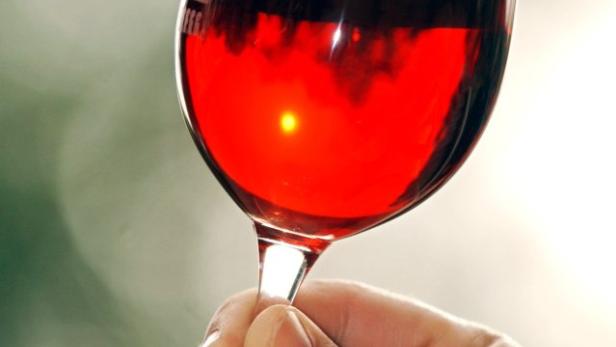 Eine Hand hält ein Glas Rotwein gegen einen hellen Hintergrund.