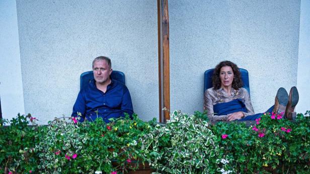 Ein Mann und eine Frau sitzen auf einem Balkon hinter einem Blumenkasten.